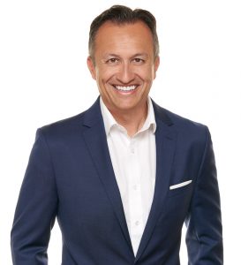 Professional headshot of a smiling man in a navy blue suit and white shirt, standing against a plain white background